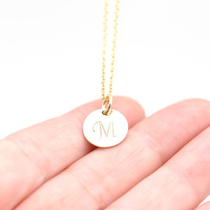 gold initial necklace shown in a hand