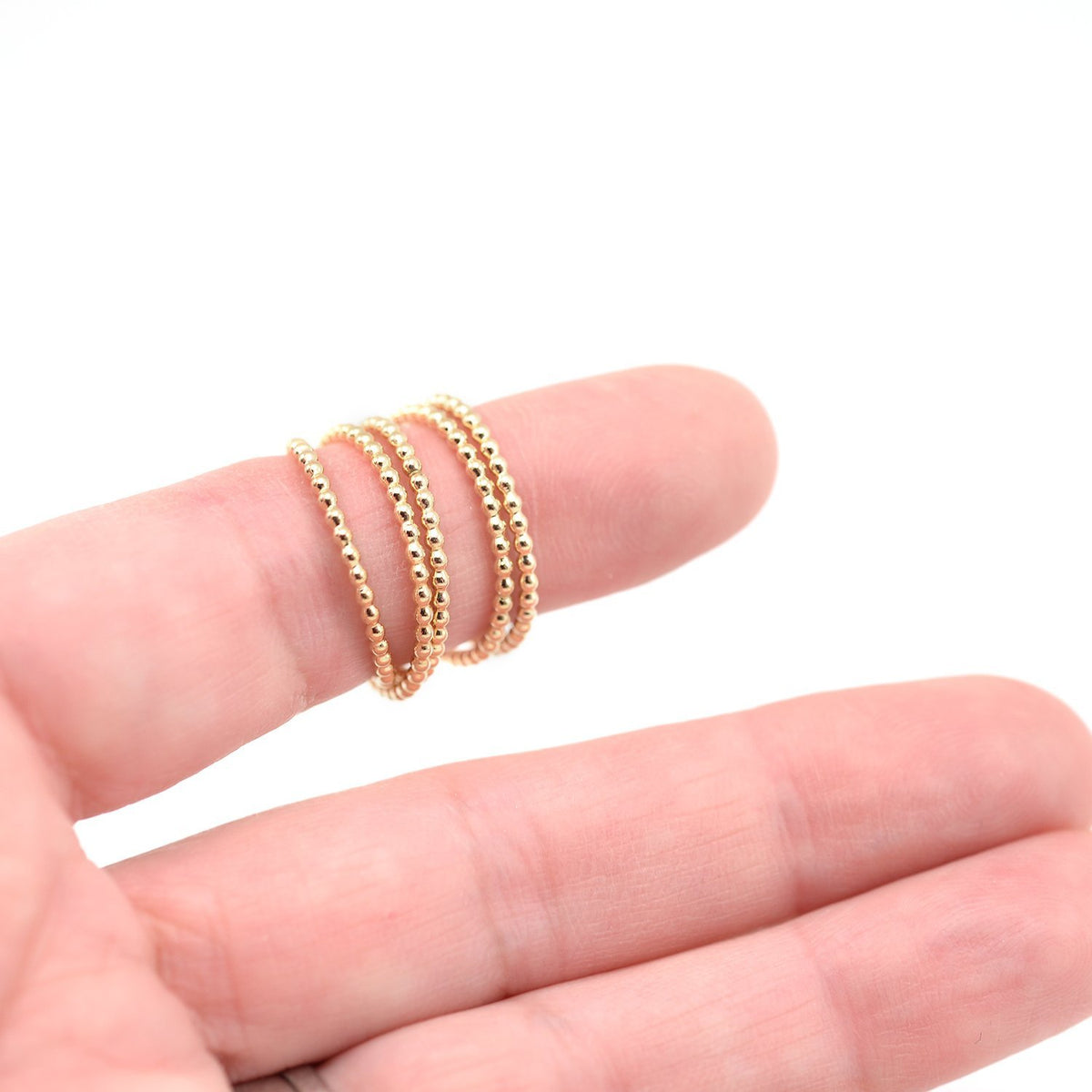 Gold stacking beaded rings on finger